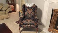 Wingback chair with floral upholstery, showing full front view in a room interior with nearby furniture.