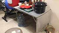 Full view of aluminum camping table showing metal surface with items on top (items not included), drop leaf on side, and folding legs.