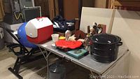 Photo showing items on table including pot, cooler, briefcase, and miscellaneous items