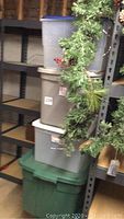 Side view of five stacked plastic storage totes in different colors near metal shelving and Christmas greenery.