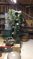 Full view of artificial Christmas trees and garland hanging on a stand with shelves in the background.