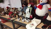 Photo showing multiple plush teddy bears and Christmas figures including snowmen and penguin on shelves, along with wooden cow figurines and a Christmas stocking.