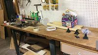 Wide shot of work table holding belt sander, mount brackets, adhesive box, spray bottles, and various tools.