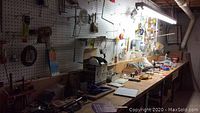 Wide view of basement workshop with pegboard wall holding tools and a workbench with various tools and supplies arranged on it.