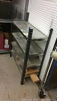 Metal shelving unit showing side profile with three shelves and framework, placed against a pegboard wall.