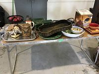 Table with assorted trays, platters, decorative ceramic pieces, metal trays, ceramic stein, statuette