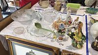 Photo showing porcelain figurines, crystal bowls, cake plate, corn holders, and candle holders arranged on a table.