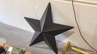 Brown painted metal star viewed from front and side showing 3D facets and wear.