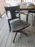 Front-side view of antique wooden office chair showing curved backrest, contoured seat, armrests, and part of the wooden floor beneath.