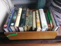 Photo showing 13 hardcover books stored in a vintage wooden office tray, titles viewable on some spines including Harper Lee's 'To Kill a Mockingbird'.