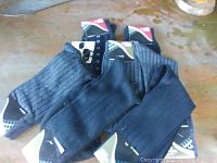 Top view of eight pairs of black and dark gray men's dress socks with tags visible, showing patterns including vertical stripes and checkered accents