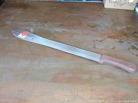 Full view of the 26 inch machete with the wooden handle laid flat on a wooden surface.