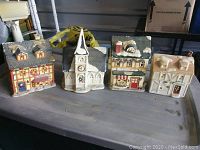 Four vintage ceramic Christmas village houses displayed on a table, showing various architectural styles including church, house, and shop