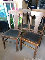 View of four wooden antique chairs with leather seats arranged together, showing the front and side angles.