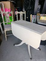 Full view of white distressed finish drop leaf dining table with two matching chairs, showing general condition and style