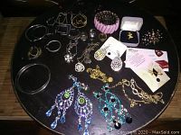 Top view of assorted costume jewelry including earrings, rings, pins, necklaces, and bangles arranged on a black plate.