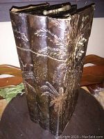 Exterior view of the metal storage box shaped like a book, showing embossed foliage designs and metal clasp closure.