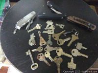 Photo of old keys and three utility knives spread out on a dark round table, showing varied types of keys and knives in used condition
