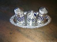 Full view of the salt and pepper shakers and small condiment jar in pierced silverplate holders on ornate silverplate tray