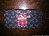 Front view of black wallet with small skull and crossbones pattern and red plaid skull applique with zipper