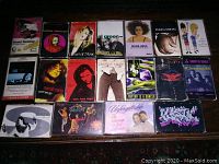 Top down photo showing 17 vintage cassette tapes laid out on a patterned carpet illustrating various artists and album covers.