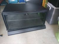 Black pivoting TV stand with closed glass doors and shelves inside, showing slight wear on surface.