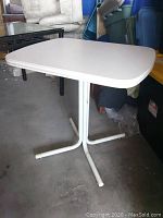 Full view of the white laminate retro kitchen table showing top and metal base against garage background.