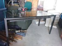 Full view of the outdoor rectangular table showing metal frame and glass top with surrounding items for scale.