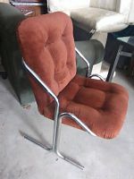 Side angled view showing the burnt orange cushioned fabric and chrome tubular frame of the retro office chair. Chair has some dust visible on the fabric from storage.