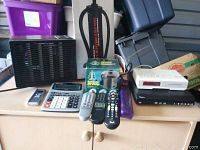 Photo showing various electronics on a wooden surface including a Woods water pump, calculator, three remote controls, small cell phone, and a boxed accessory.