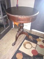 Full view of the round wood table on a carpet with three paw feet visible, showing the single central column and one of the four drawers.