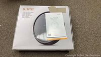 Boxed iLife robotic vacuum with user manual taped on top of the box.