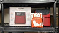 Photo showing the Cosori air fryer next to its box and recipe booklet on a shelf.