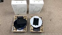 Two Eufy RoboVac 11S units in foam trays with chargers and boxes behind