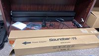 Soundbar Y6 in box with included remote, cables, and power adaptor on shelf