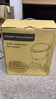 Closed cardboard box labeled Honey Guardian A36 Automatic Pet Feeder showing key features like durable quality, healthy diet, precise feed, safety and efficiency.