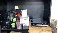 Shelf displaying all items in the lot including Aicok juicer, Daze tea pot in box, handheld juicer cup, and Duxtop induction cooktop.