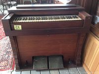 Front view of wooden pump organ showing keyboard with aged keys and wooden casing.