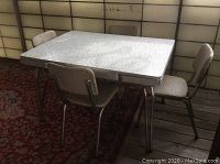 Front side view of the vintage Arborite table with four chairs set around it, on a patterned carpet.