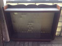 Front view of vintage wooden showcase cabinet with clear glass sliding doors and scalloped wood top edge