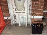 Photo showing metal wine rack, leaded painted window, metal shower organizer, and garbage bins with wooden hangers arranged on a porch