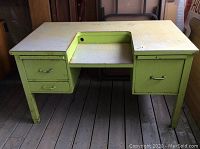 Front-left angle view of the desk showing green metal drawers on the left side, white top surface with texture, and metal legs.