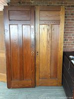 Pair of two wooden three-panel doors leaning against brick wall. Both doors are solid wood with keyholes but no hardware attached, showing natural finish and wood grain.