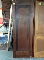 Dark stained one panel solid wood door leaning against wall with brick background