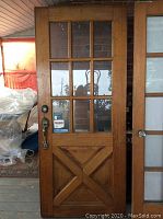 Full view of wooden entrance door showing nine glass panels with one broken and the cross-patterned wooden lower half