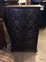 Closed view of the retro wooden bar cabinet with carved pocket doors and decorative handles.