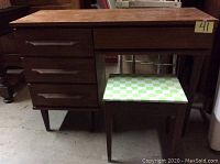 Full frontal view of the teak desk with four drawers on the left and stool tucked underneath showing overall condition and design.