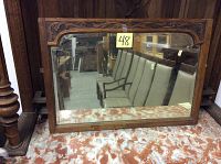 Front view of the antique carved oak mirror showing the overall condition and detailed carvings on the top corners of the frame with beveled glass reflecting chairs in the background.
