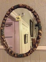 Oval wall mirror with Louis XVI style painted rose floral frame shown hanging reflecting interior room.