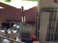 Photo showing a selection of the lot items including two metal doors leaning against the wall, a vintage plaid cooler on the floor, red gas tank, tool box, and multiple metallic and electrical parts including industrial light fixtures with transformers.